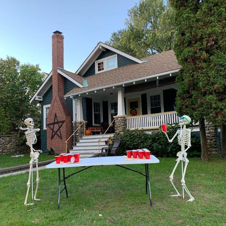 two skeletons playing table tennis in front of a house with halloween decorations on the lawn