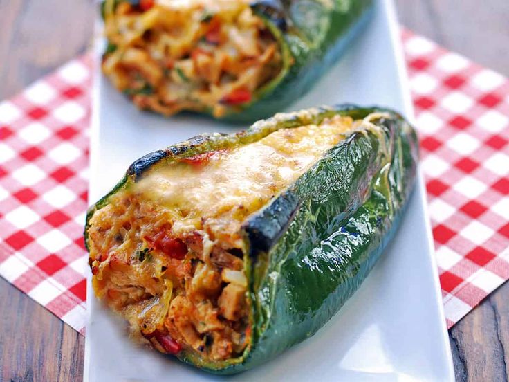 two stuffed peppers on a white plate with a red and white checkered tablecloth