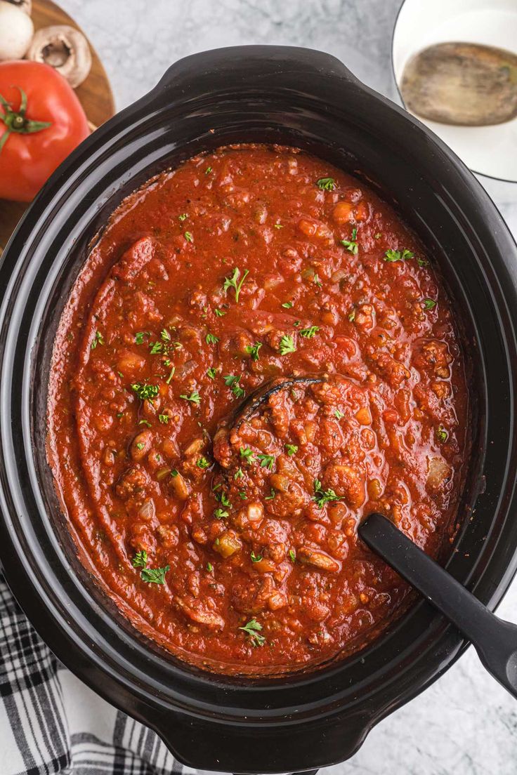 a slow cooker filled with chili sauce and garnished with fresh parsley