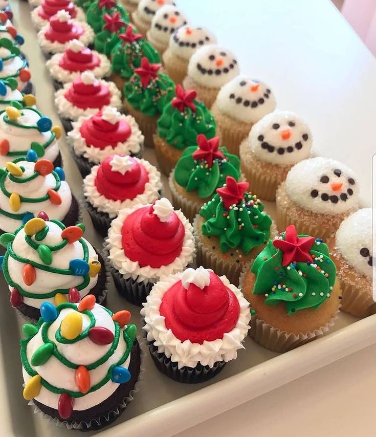 cupcakes decorated with frosting and decorations are lined up on a white tray