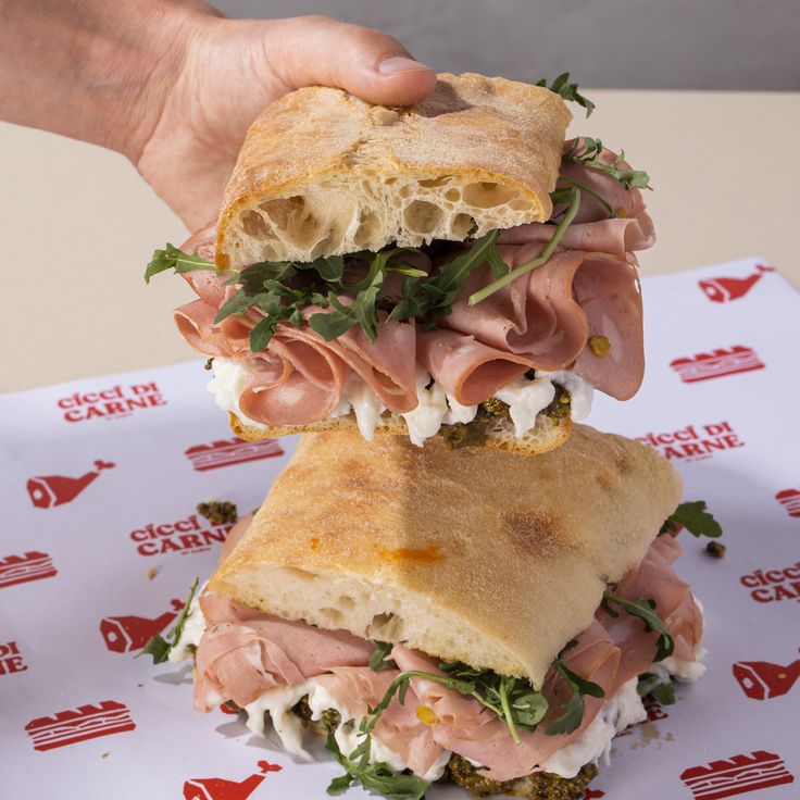 two sandwiches stacked on top of each other in front of a person's hand