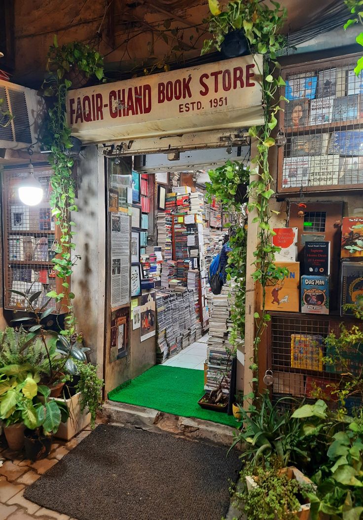 an open book store with lots of books on the wall and plants growing around it