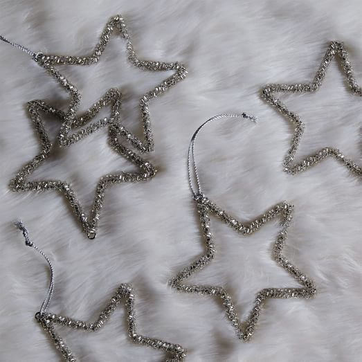 three silver stars are laying on a white fur covered surface, one is hanging from the ceiling