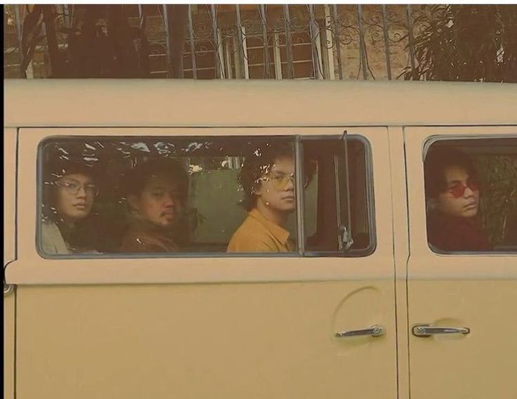 three people are sitting in the passenger seat of a yellow van, looking out the window