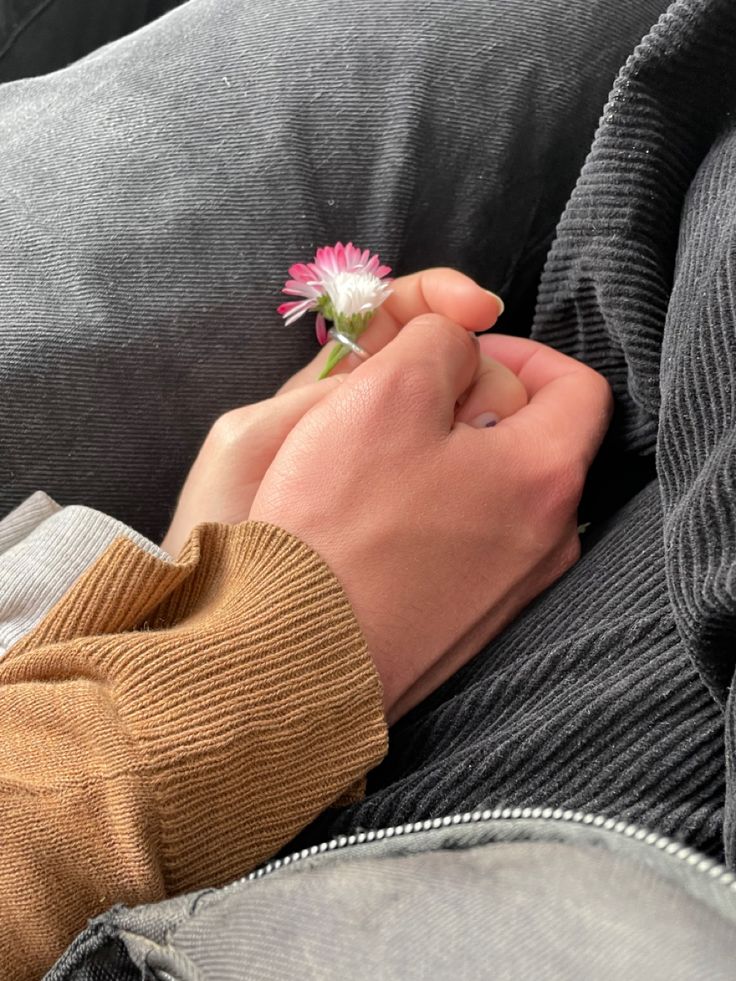 a person holding a flower in their left hand while sitting on a couch with his arm wrapped around him