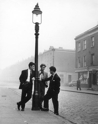 three men in suits standing next to a lamp post