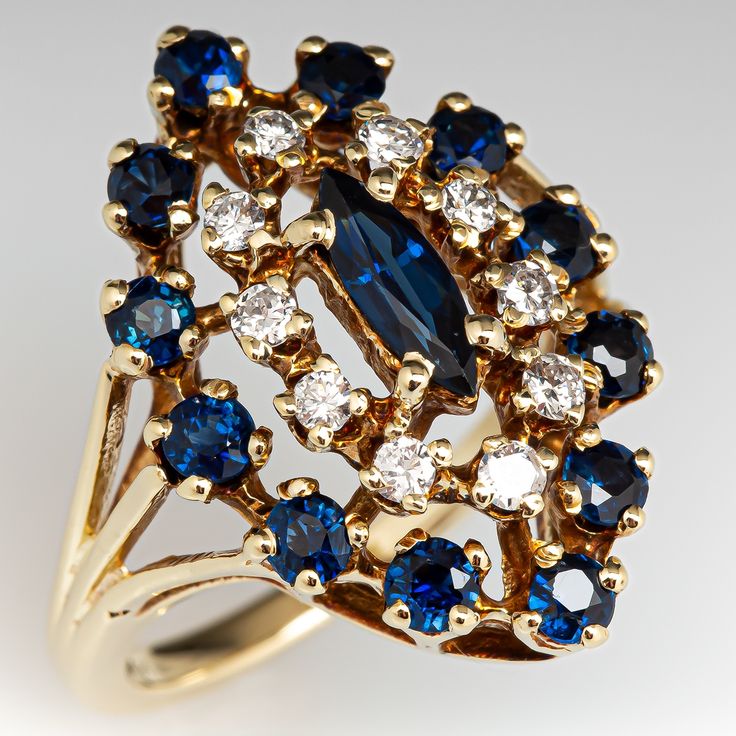 This elegant ring is centered with one (1) marquise mixed cut natural sapphire set into a four-prong setting and is bordered with ten (10), prong set, round brilliant cut diamonds and twelve (12), prong set, round mixed cut natural sapphires. The ring measures 23.0mm at the top, rises 9.4mm above the finger, tapering to 1.9mm wide and 1.5mm thick at the base of the shank. This ring is currently a size 6 1/8. Elegant Marquise Cut Multi-stone Cluster Ring, Sapphire Marquise Diamond Ring, Marquise Sapphire Ring With Brilliant Cut, Marquise Cut Sapphire Ring For Anniversary, Marquise Sapphire Ring For Formal Occasions, Sapphire Ring With Diamond Accents And Marquise Cut, Anniversary Multi-stone Marquise Cut Sapphire Ring, Anniversary Sapphire Ring Marquise Cut Multi-stone, Marquise Cut Multi-stone Sapphire Ring For Anniversary