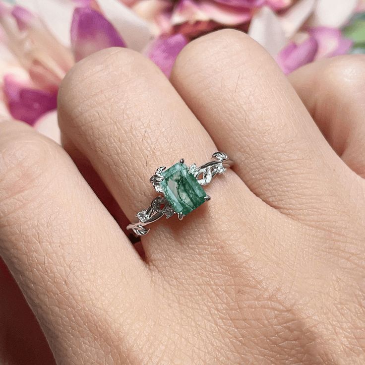 Connect with the grounding energy of the Earth Moss Agate Ring, inspired by the element of earth. This piece showcases an emerald-cut moss agate center stone, symbolizing growth and harmony with nature. The intricate leaves surrounding it, adorned with shining white topaz, pay homage to the natural beauty and tranquility of the earth. Wear this ring as a reminder to stay rooted, find balance, and celebrate the beauty of the natural world. ✦ 14K white gold vermeil (14K white gold plated over a st Green Emerald-cut Gemstone Accent Jewelry, Green Emerald Cut Jewelry With Gemstone Accents, Emerald Cut Green Gemstone Jewelry, Nature-inspired Green Oval Emerald Ring, Emerald Cut Tourmaline Jewelry With Accent Stones, Green Crystal Gemstone Ring For Spiritual Wear, Green Emerald Crystal Ring With Accent Stones, Emerald Crystal Ring With Accent Stones, Green Emerald Cut Crystal Birthstone Ring