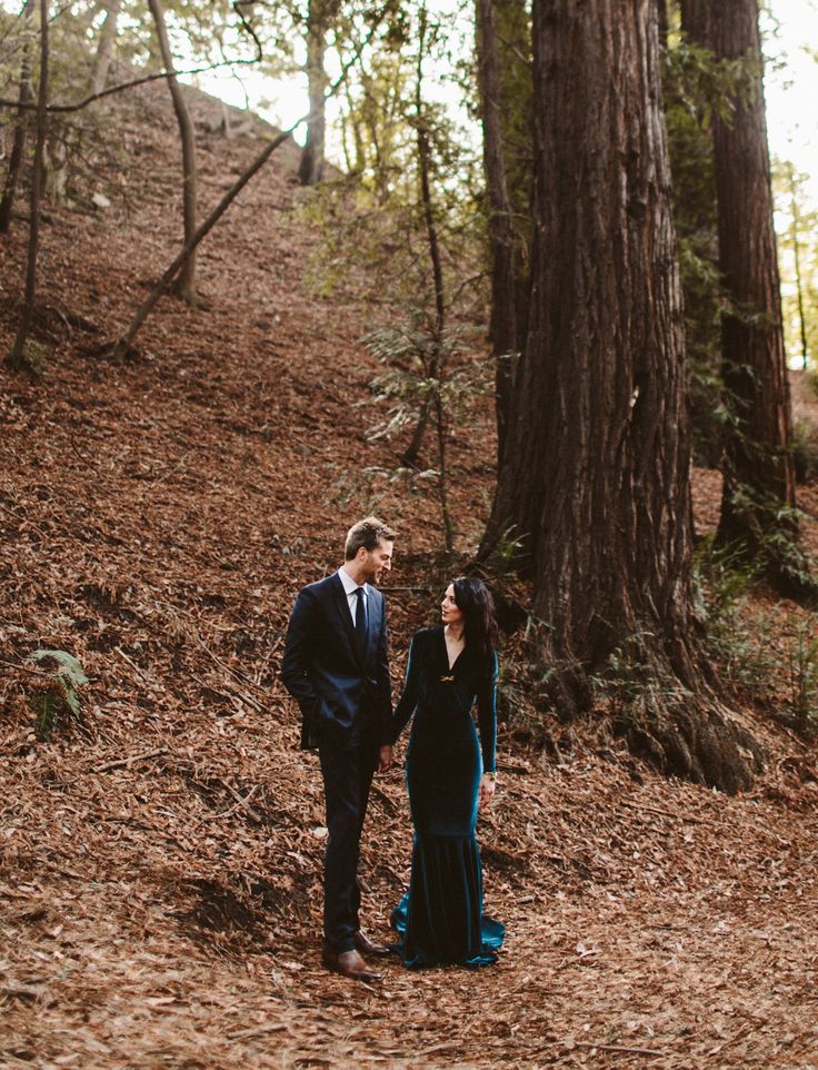 a man and woman standing next to each other in the woods