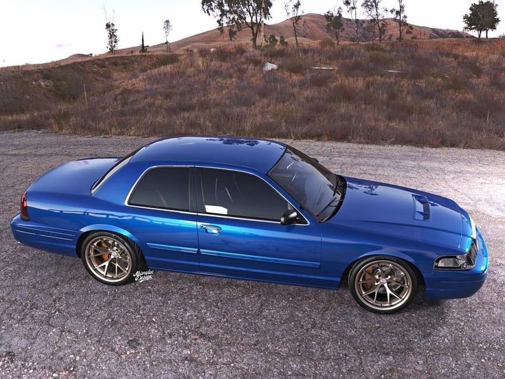 a blue car parked on top of a gravel covered parking lot next to a hill