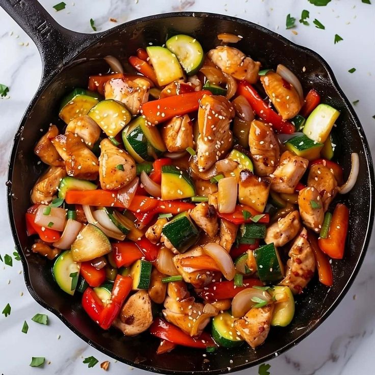 a skillet filled with chicken, vegetables and sauce on top of a marble counter