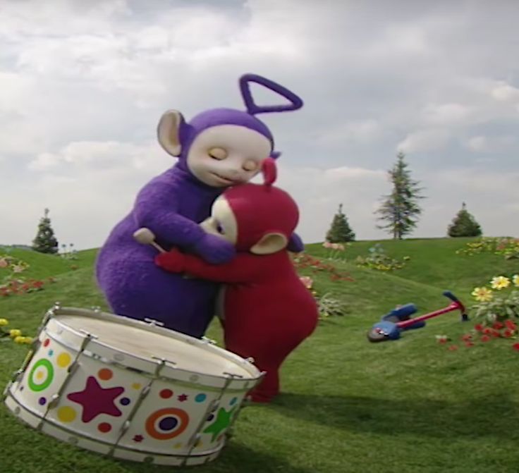 two stuffed animals hugging each other in front of a drum on the grass with flowers behind them