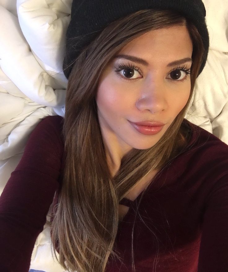 a woman laying on top of a bed wearing a black beanie and looking at the camera