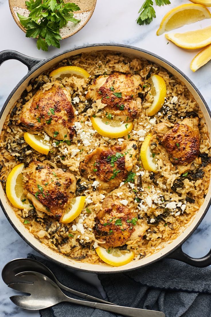 chicken and rice with lemons in a skillet on a marble countertop next to silverware