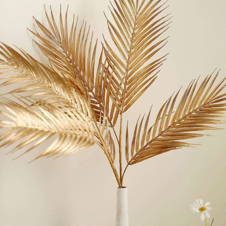 a white vase filled with lots of gold colored leaves and flowers on top of a table