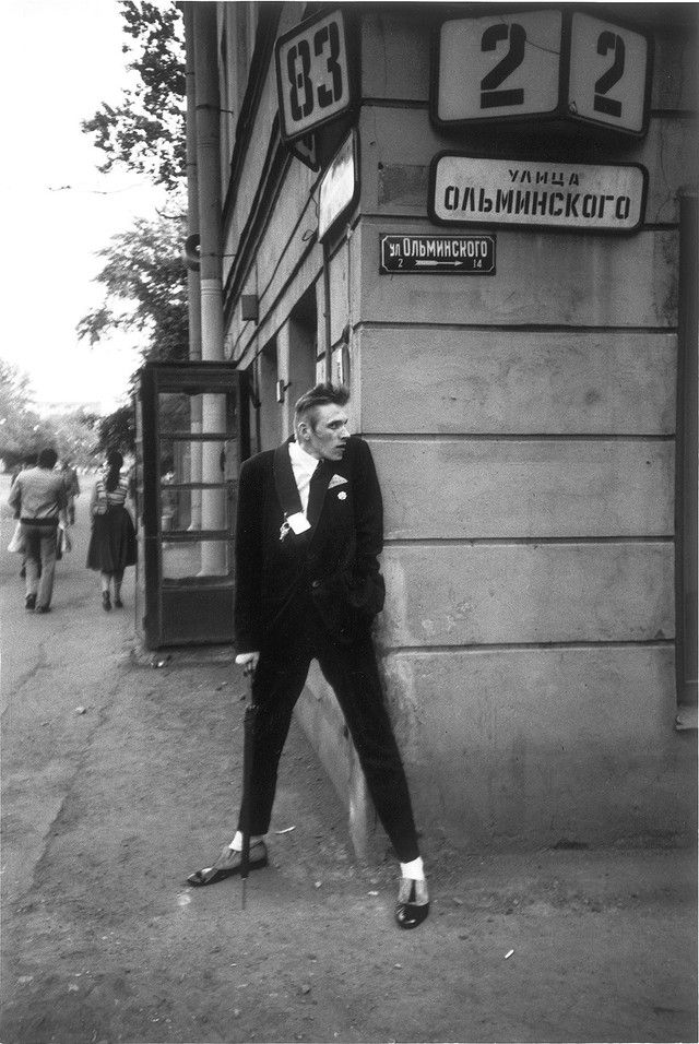 black and white photograph of a man leaning against a wall in front of a building