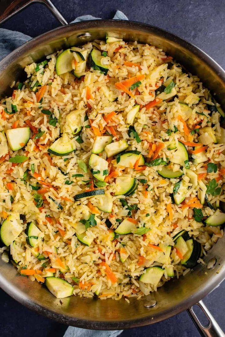 a pan filled with rice, zucchini and carrots on top of a table