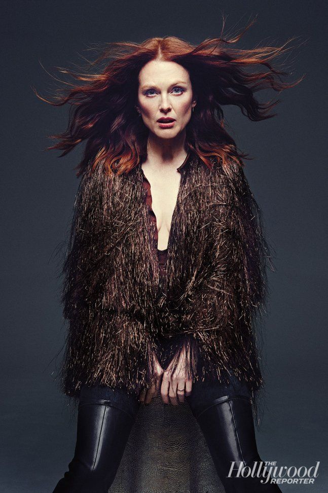 a woman with red hair sitting on top of a chair wearing black leather pants and a brown jacket