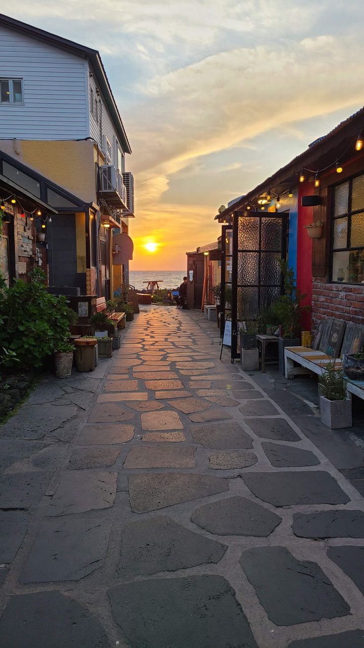 the sun is setting on an empty street with benches and tables in front of it