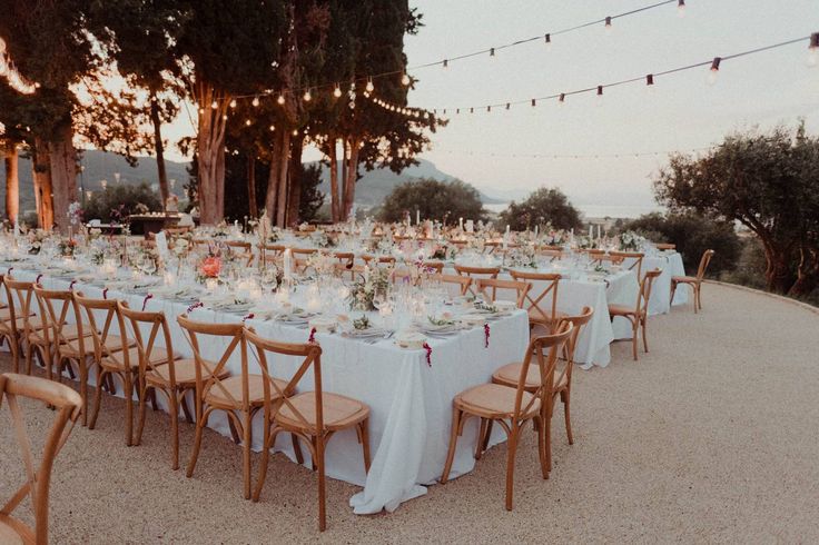 a long table is set up with white linens and place settings for an outdoor dinner