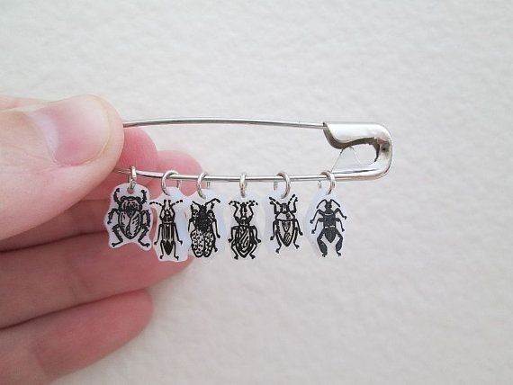 a hand holding a silver tie bar with four bugs on it and three smaller ones hanging from the end