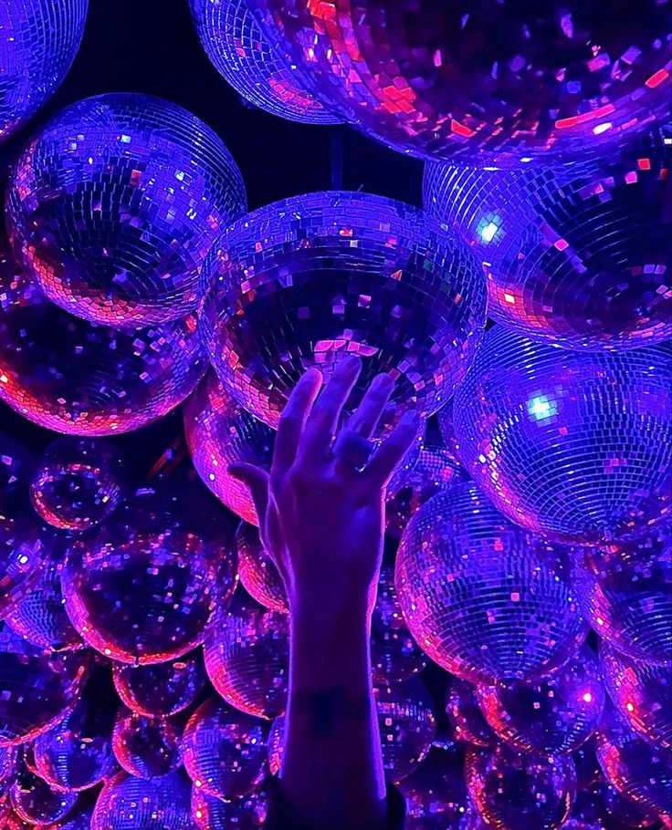 a person reaching up to some shiny disco balls in the air with their hands on them