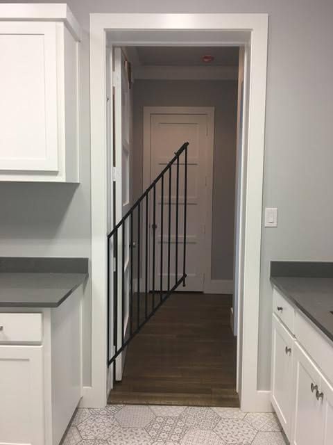 an open door leading to a kitchen with white cabinets and black handrails on the wall