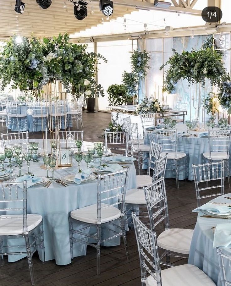 tables and chairs are set up for an event with blue linens, white tablecloths and greenery