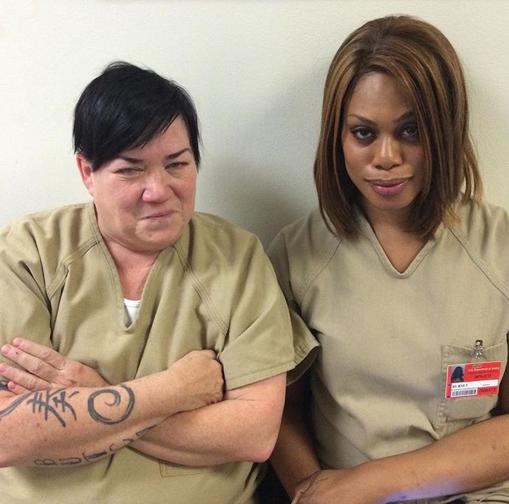 two women sitting next to each other with tattoos on their arms and hands, one woman has her arm around the man's shoulder