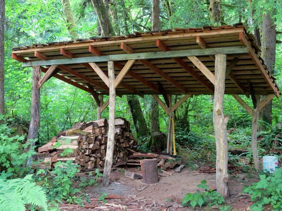 a wooden shelter in the middle of a forest with logs stacked on top of it