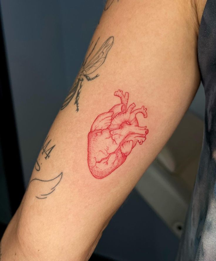 a red heart tattoo on the arm of a man with dragonflies around his neck