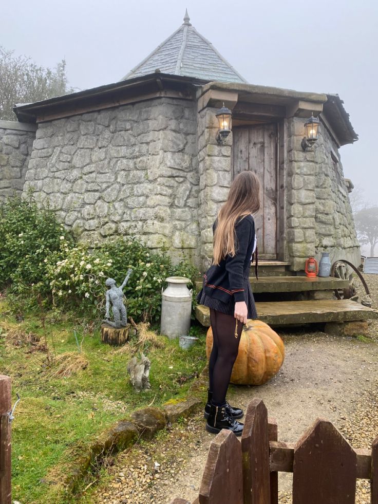 a woman sitting on top of a wooden bench next to a stone building and pumpkins