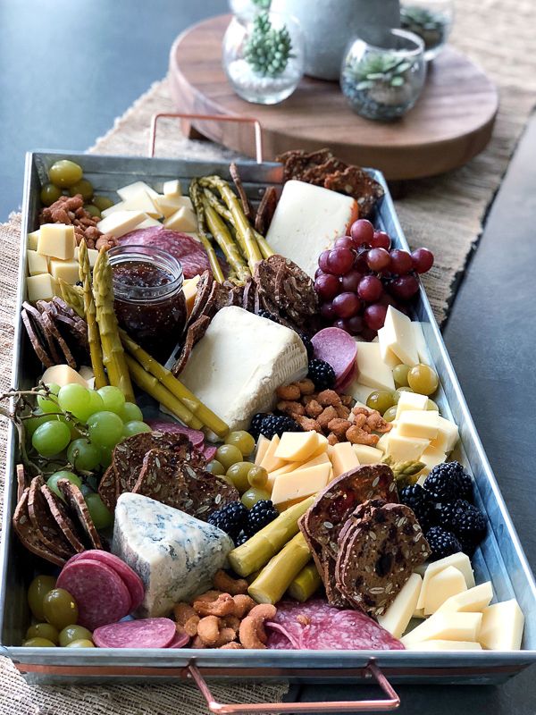 a metal tray filled with different types of cheeses and grapes next to a glass of wine