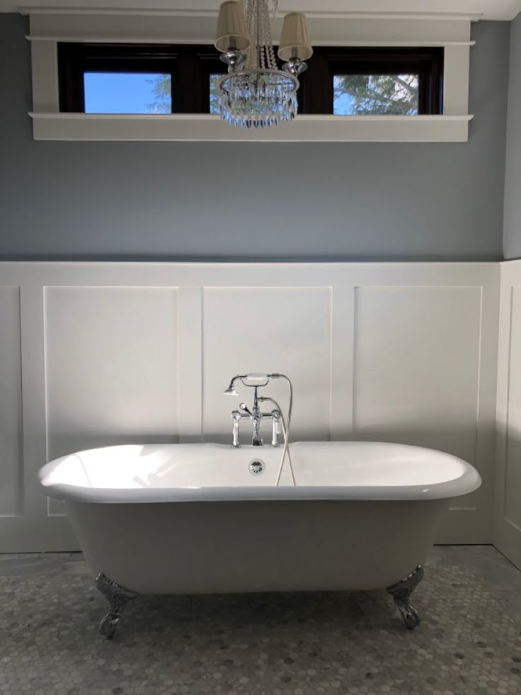 a white bath tub sitting in a bathroom next to a window with a chandelier hanging above it