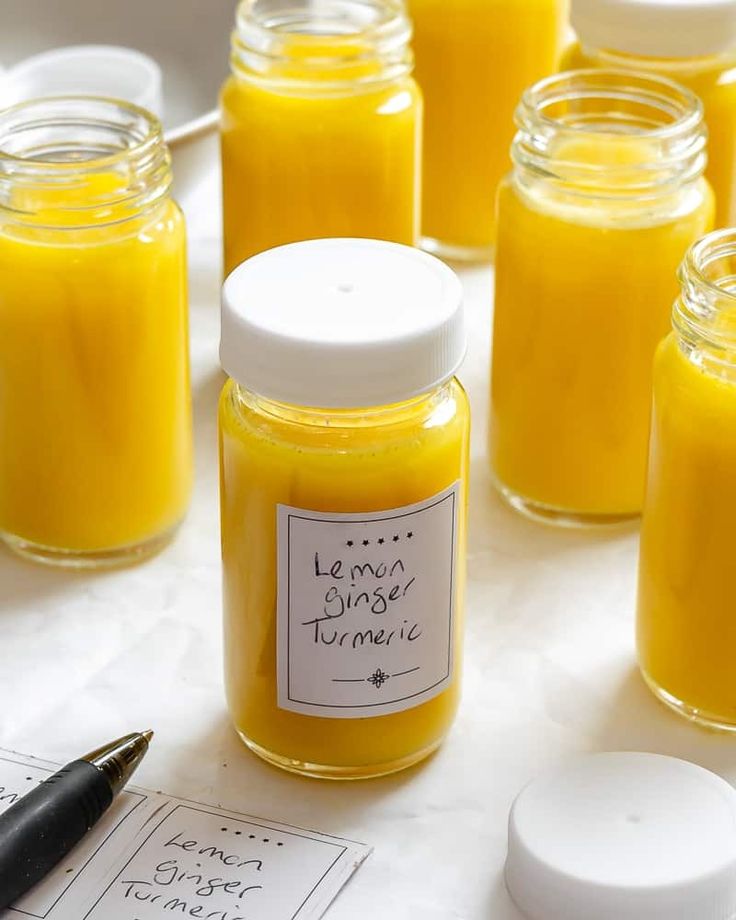 several jars filled with yellow liquid sitting on top of a table next to a pen