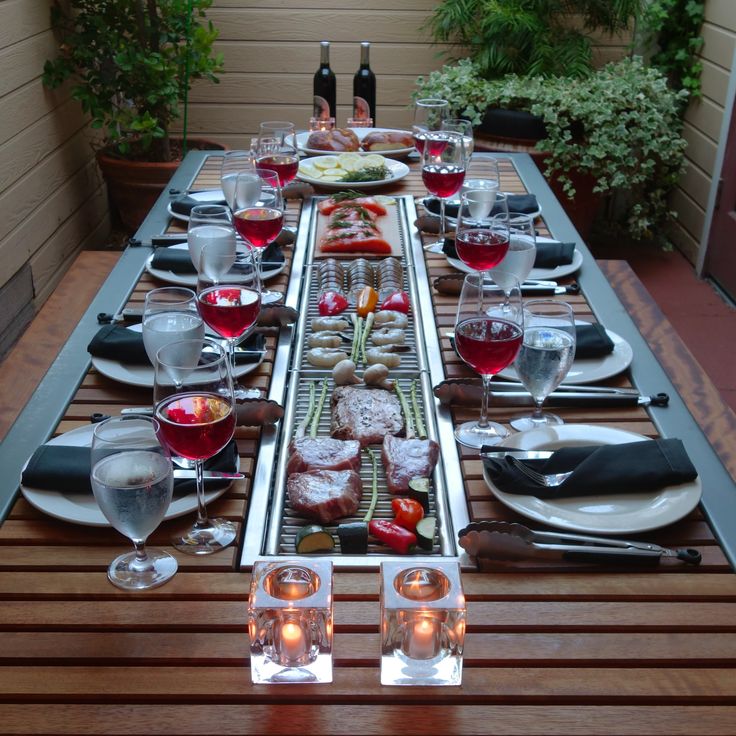 a long table is set with food and wine for two people to enjoy on an outdoor patio