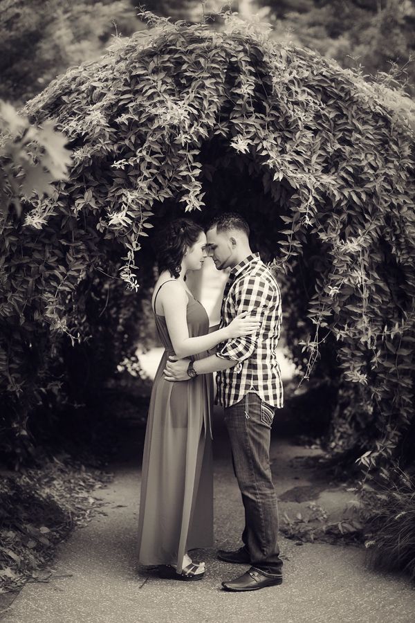 a man and woman standing in front of an archway with trees on either side holding each other