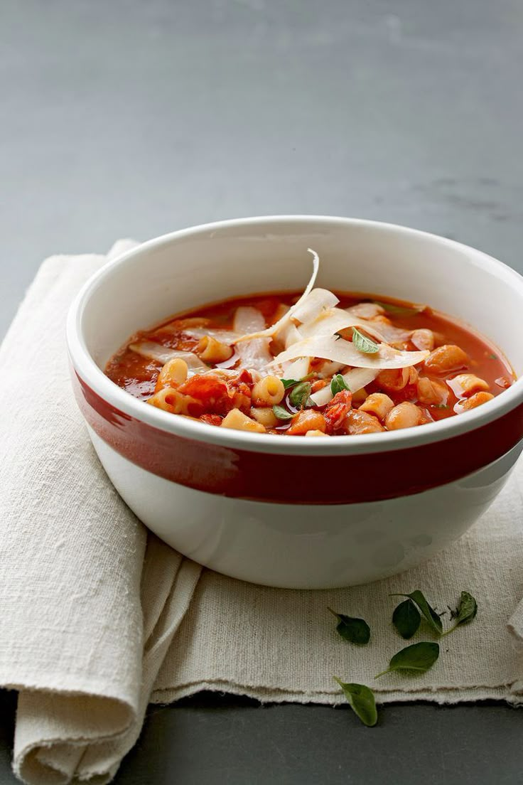 a red and white bowl filled with soup on top of a cloth next to a napkin