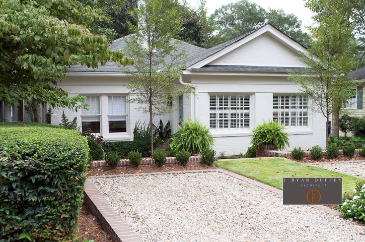 a white house with trees and bushes around the front yard, along with a gravel path leading to it