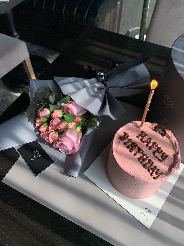 a pink birthday cake with a candle on it next to a bouquet of roses and a card