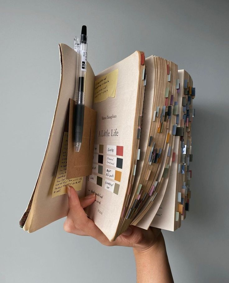 a hand holding an open book with many pages and a pen sticking out of it