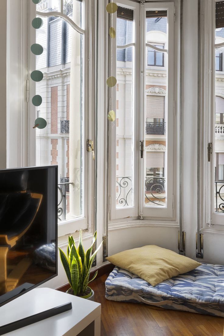 a dog bed in the corner of a living room with large windows and wooden floors