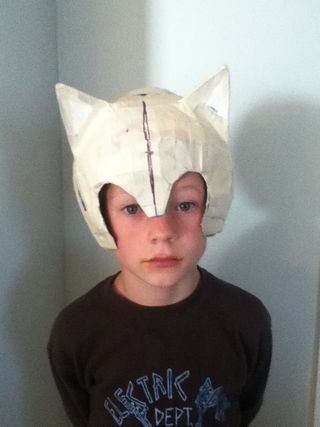 a young boy wearing a paper mache cat mask on top of his head and looking at the camera