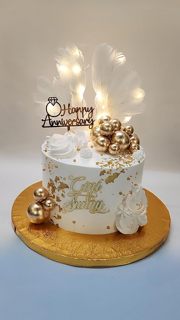 a white and gold birthday cake with some lights on it's top, sitting on a golden platter