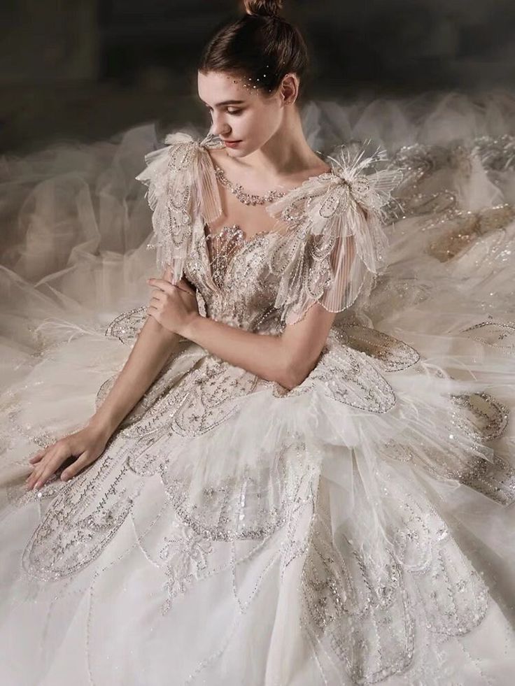 a woman in a white dress sitting on the ground with her hand on her chest