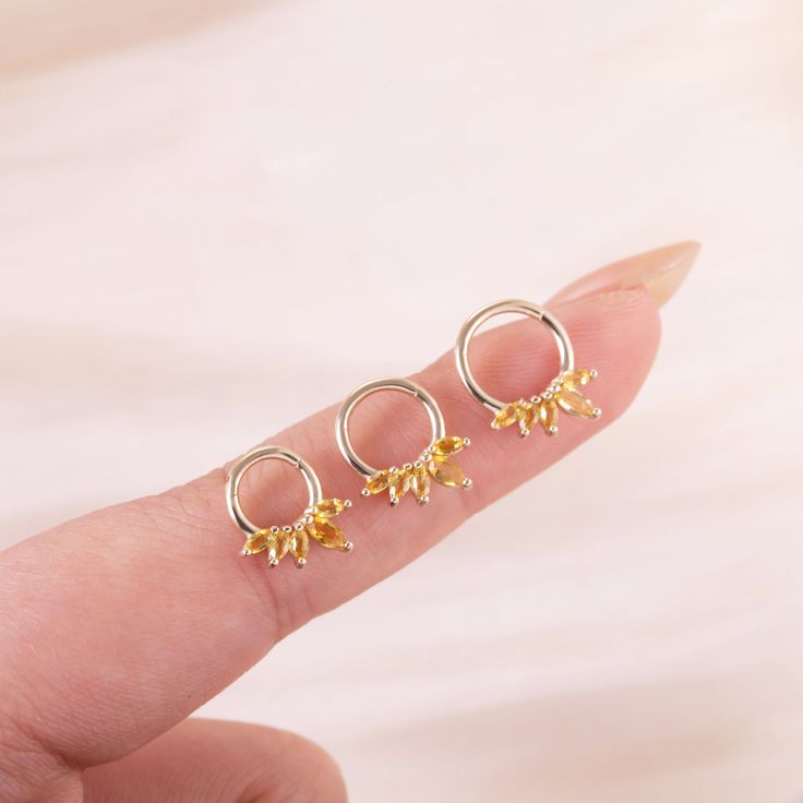 the tiny gold earrings are sitting on someone's finger