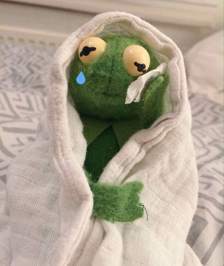 a green stuffed animal wrapped in a white towel on top of a bed with eyes and nose