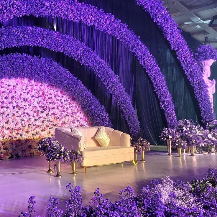 a stage set up with purple flowers and couches for a wedding or special event