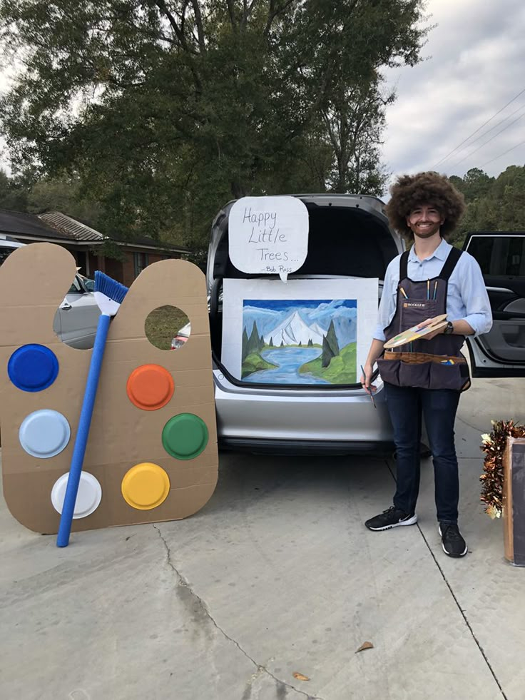 a woman standing next to a car with an art display on the back door and another vehicle behind her