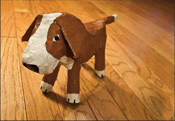 a brown and white dog made out of toilet paper on a wooden floor with wood floors